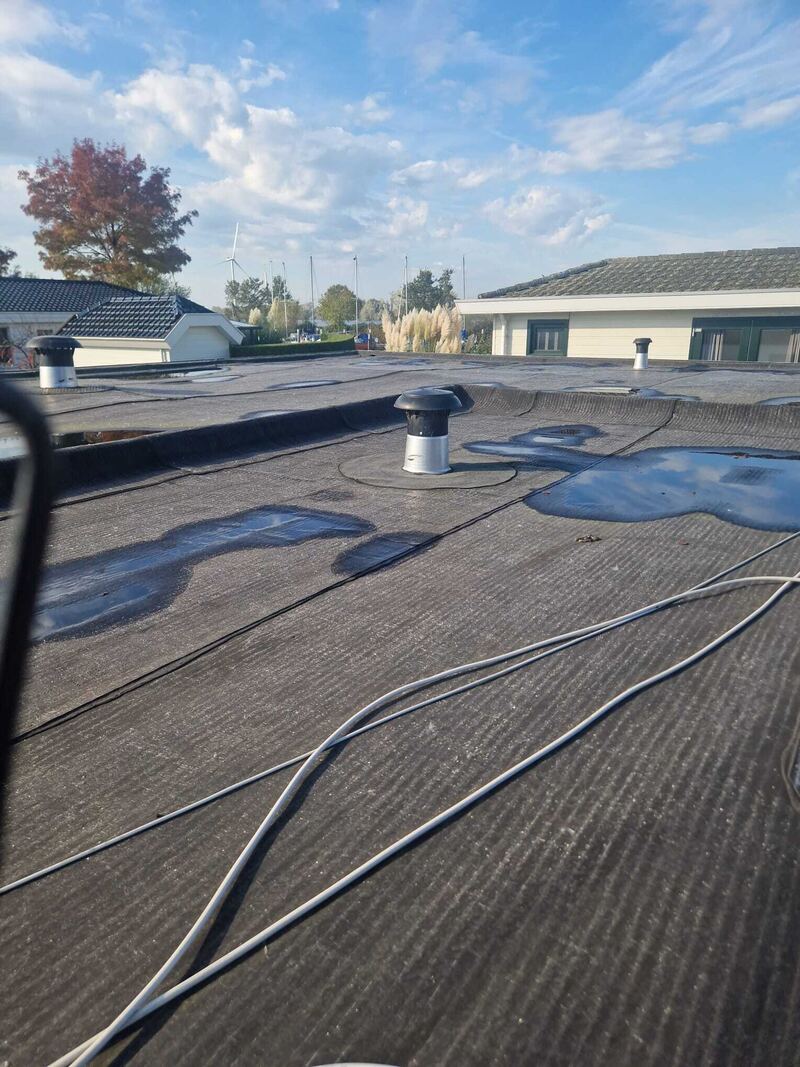 Plat dak met waterplassen en een ventilatiepijp