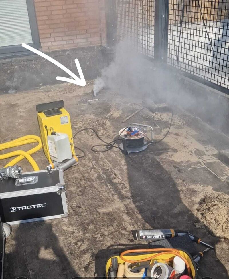 Rook komt omhoog bij een balkonhek op een dak, een pijl wijst de plek aan