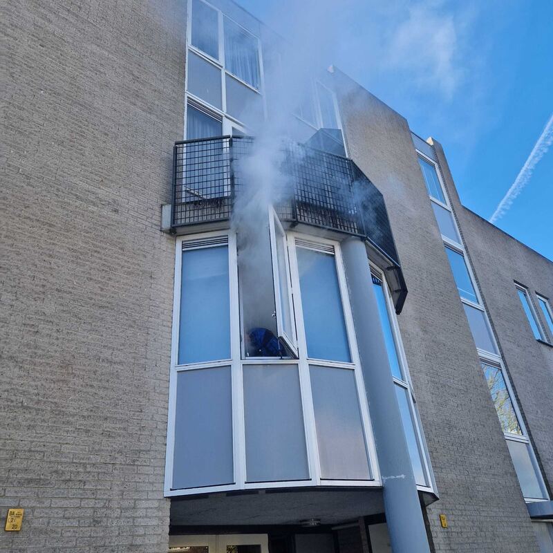 Rook komt uit een raam bij een balkon in een bakstenen gevel