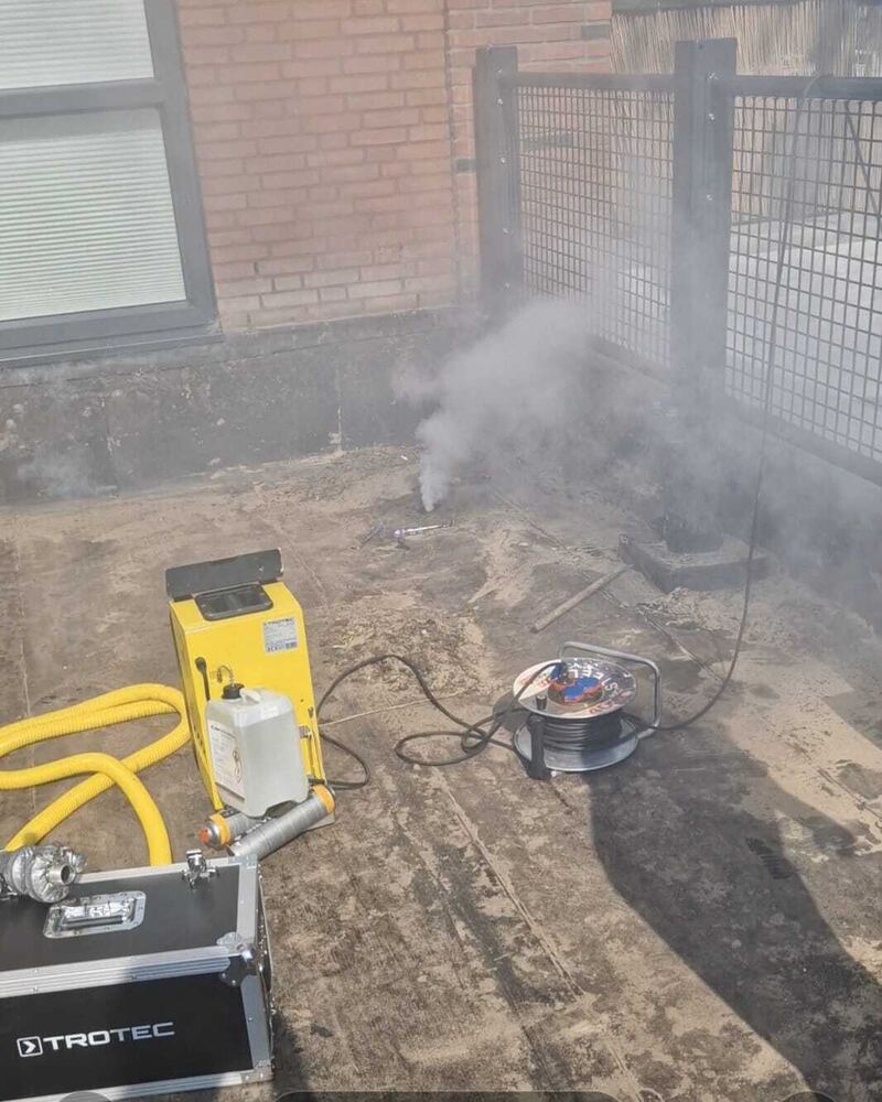 Rookmachine en gereedschapskoffer op een dak bij een hekwerk