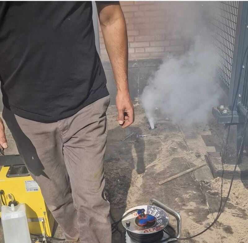 Specialist bij een rookbron naast een hekwerk op een dak