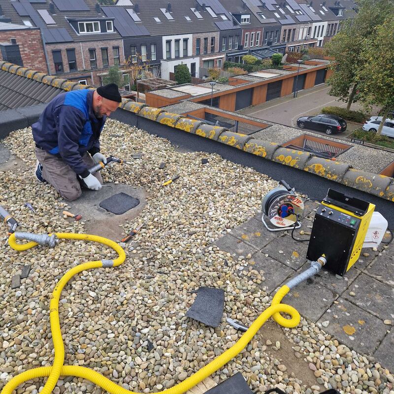 Specialist knielt bij een rookmachine op een dak met grind
