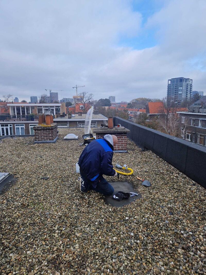 Specialist met rookmachine op een dak met grind en schoorsteen