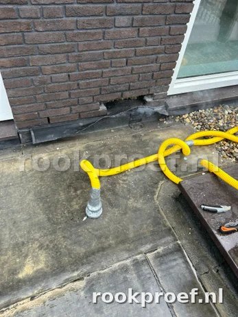 Gele rookslang bij gevelaansluiting — rook ontsnapt via lekkage naast kozijn tijdens rookproef