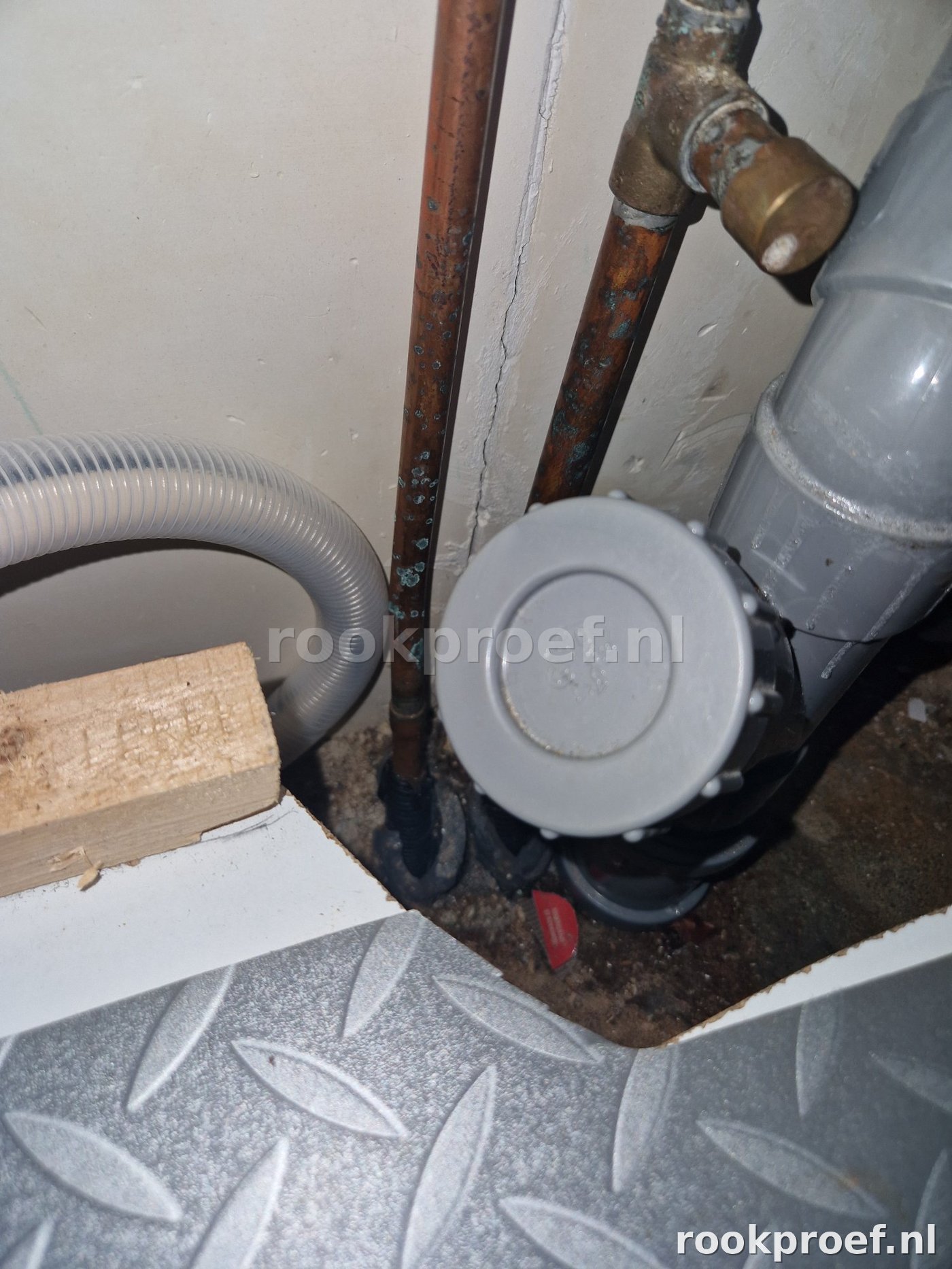 Riool afvoerknooppunt met PVC reinigingsplug en gecorrodeerde koperen leidingen na rookproef