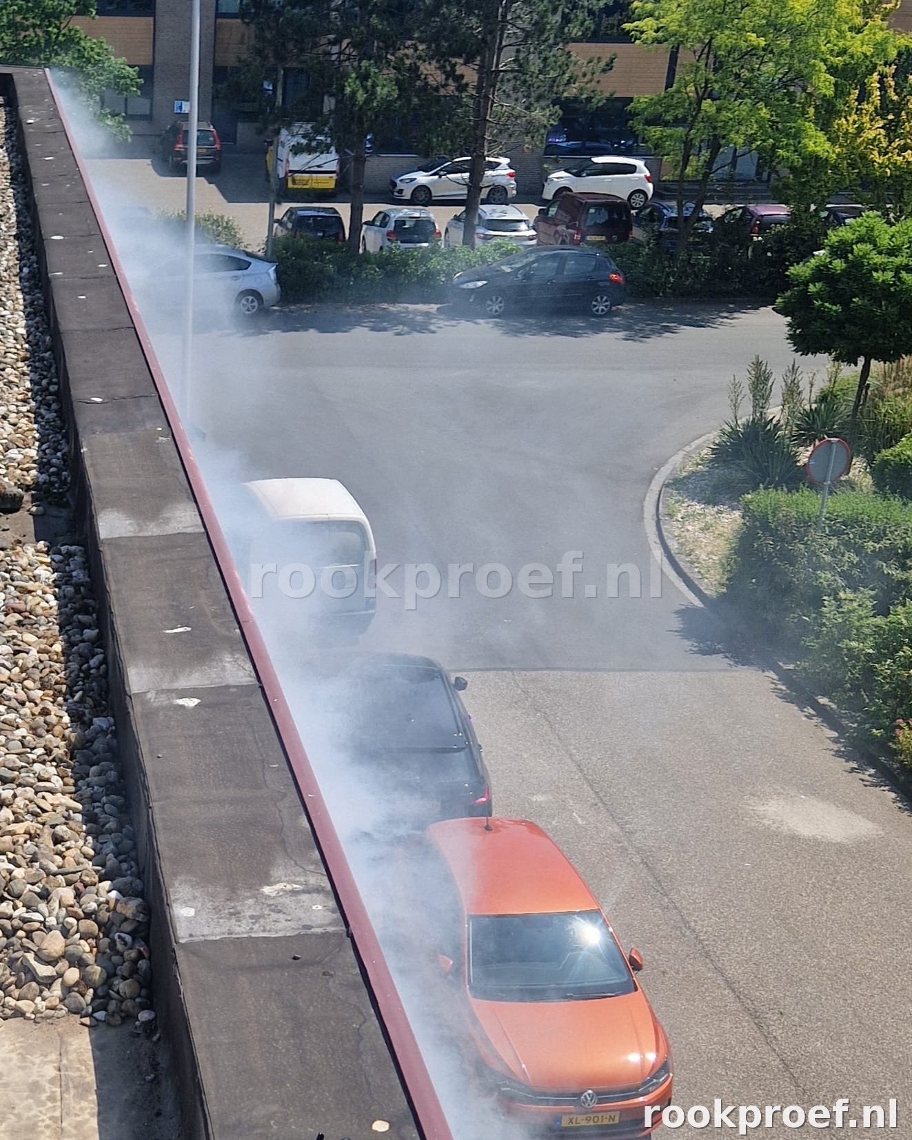 Rookgas ontsnapt via dakrand van bedrijfspand op hoogte — wolken trekken over parkeerplaats