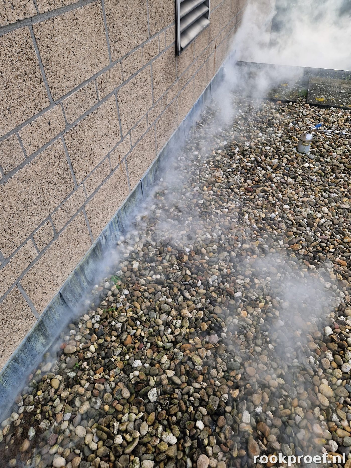 Rook ontsnapt langs volledige dakrandaansluiting bij gevel op grindlaag — lekpunt daklekkage via rookproef