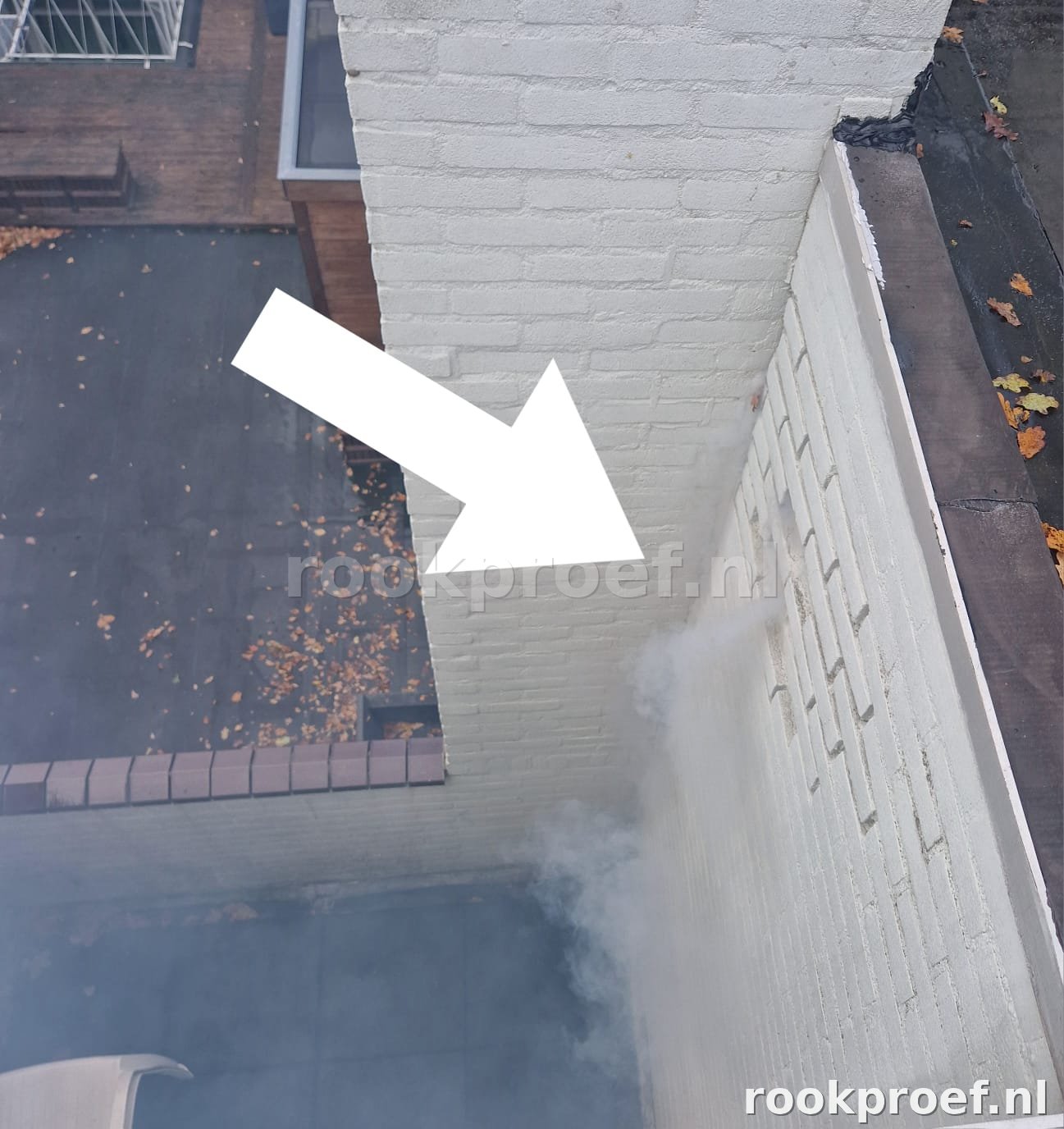 Rook ontsnapt via lekpunt in gevelmuur naast dak — witte pijl wijst exact lekpunt aan via rookproef