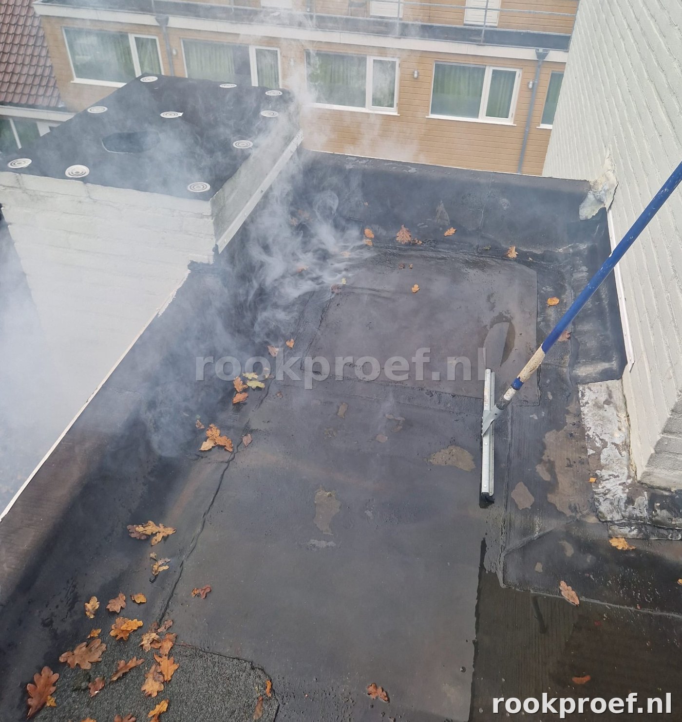 Rookgas verspreidt zich over bitumen plat dak — meerdere lekpunten zichtbaar in dakbedekking
