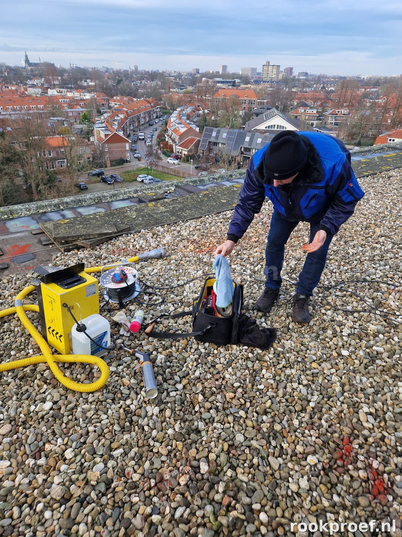 Rookproef Nederland technicus in blauw jack bereidt inspectie voor op hoog plat dak boven Leiden