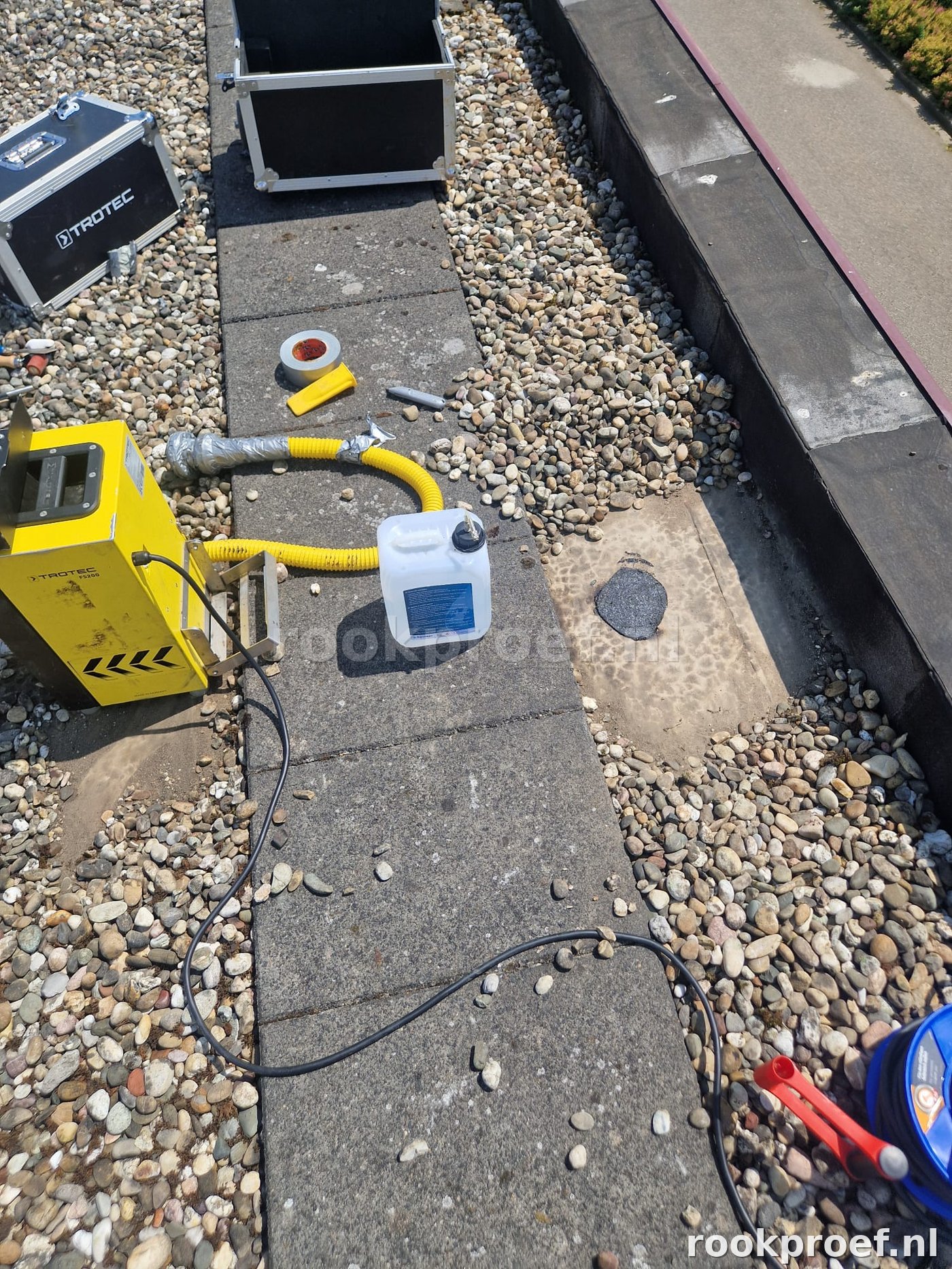 TROTEC rookgenerator opstelling op grindlaag plat dak — gele slang gereed voor daklekkage test